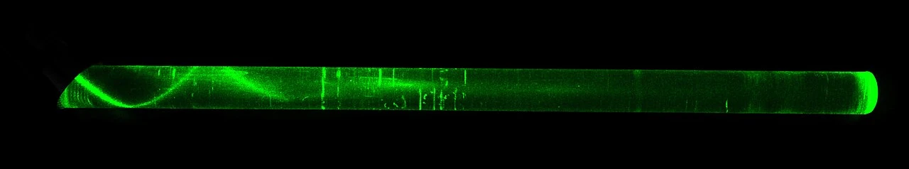 Green laser light zigzagging through a glass rod in the dark